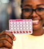 Image of a smiling woman holding up a pack of 28 oral contraceptives